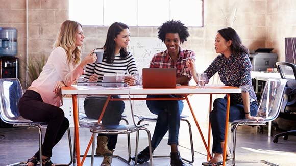 mujeres jóvenes en una reunión informal con un ordenador portátil cuatro mujeres jóvenes sentadas alrededor de una mesa en una reunión informal con un ordenador portátil