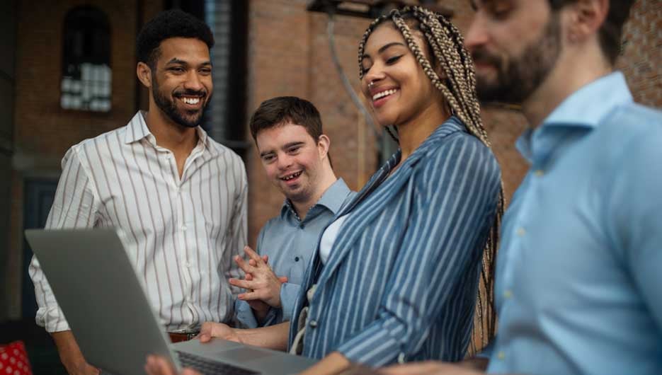 Cheerful young businesspeople with laptop working in office, social inclusion and a cooperation concept.