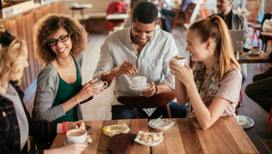 Young and diverse group of friends having a conversation over some coffee and desserts in a cafe